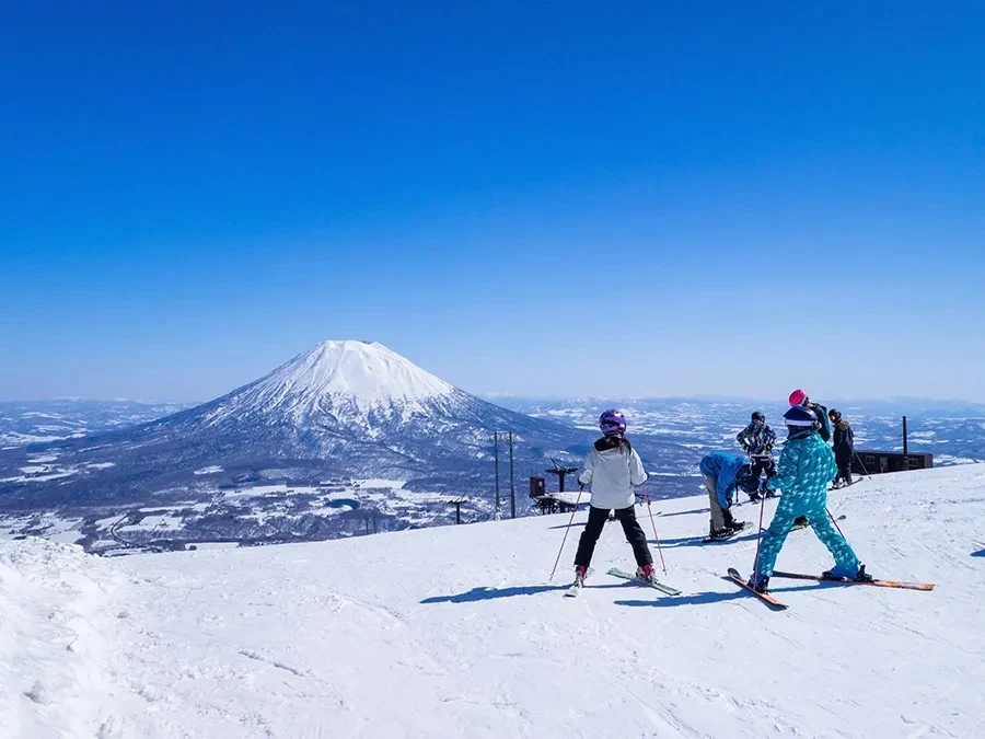 春先の晴れた日のスキー場で羊蹄山を眺めるスキーヤー達 (ニセコ、北海道)